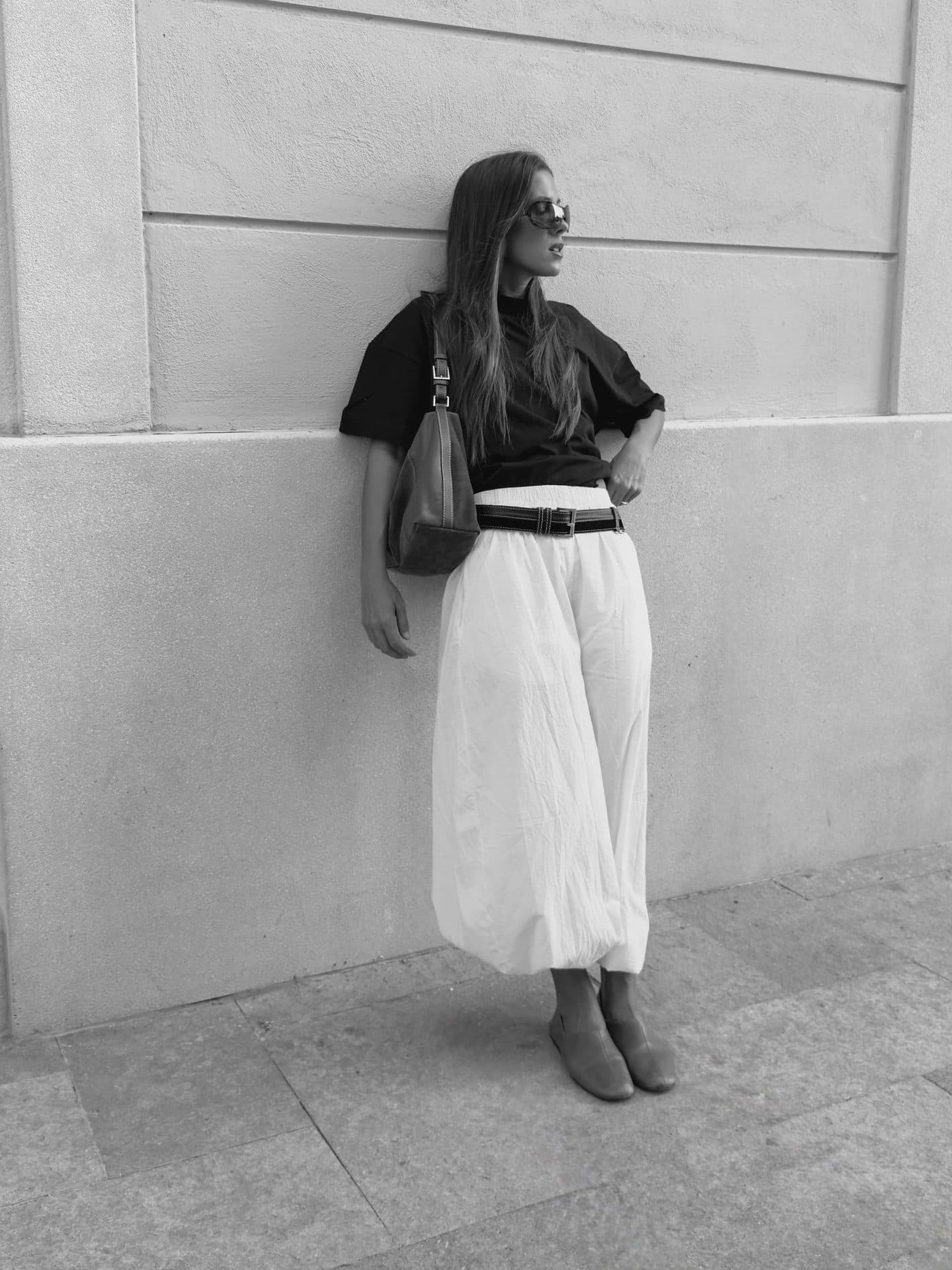 Belen Gonzalez Castellanos leaning against a textured wall, wearing a black top and wide-leg white trousers