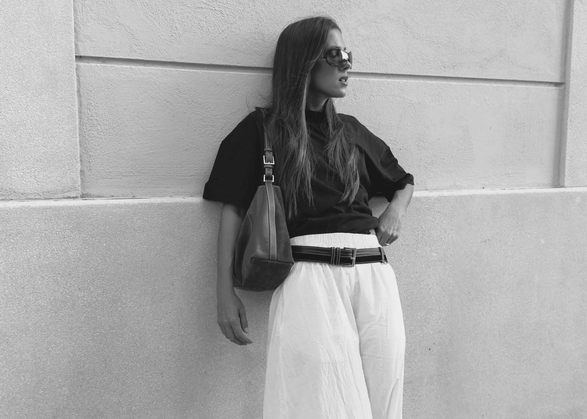 Belen Gonzalez Castellanos leaning against a textured wall, wearing a black top and wide-leg white trousers